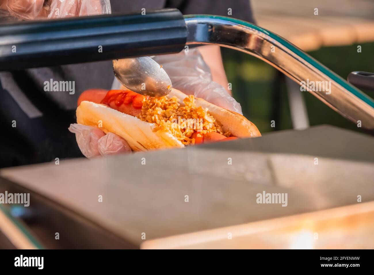Frischer Hot Dog mit gebratener Wurst, serviert in einem Café im Freien. Kochen amerikanischer Grillgerichte. Der Koch füllt einen Hot Dog mit Füllung. Grillfest Stockfoto