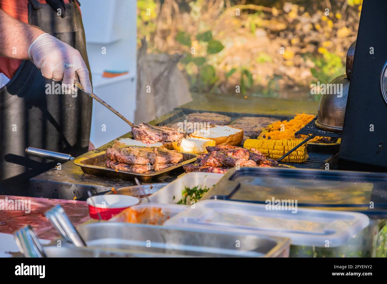 Kochen eines Burger aus den Zutaten. Ein professioneller Koch bereitet einen Burger zu. Grillfest im Stadtpark. Street Fast Food. Stockfoto