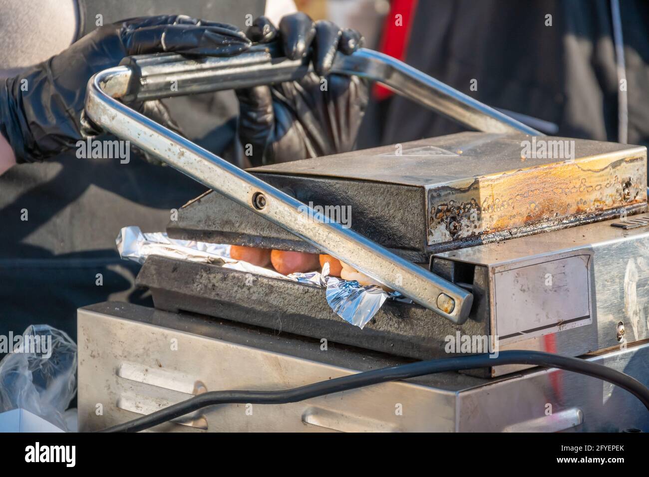 Der Koch nimmt eine auf einem rotierenden Schweißgerät gebratene Hot-Dog-Wurst. Grillfest im Stadtpark. Street Fast Food. Stockfoto