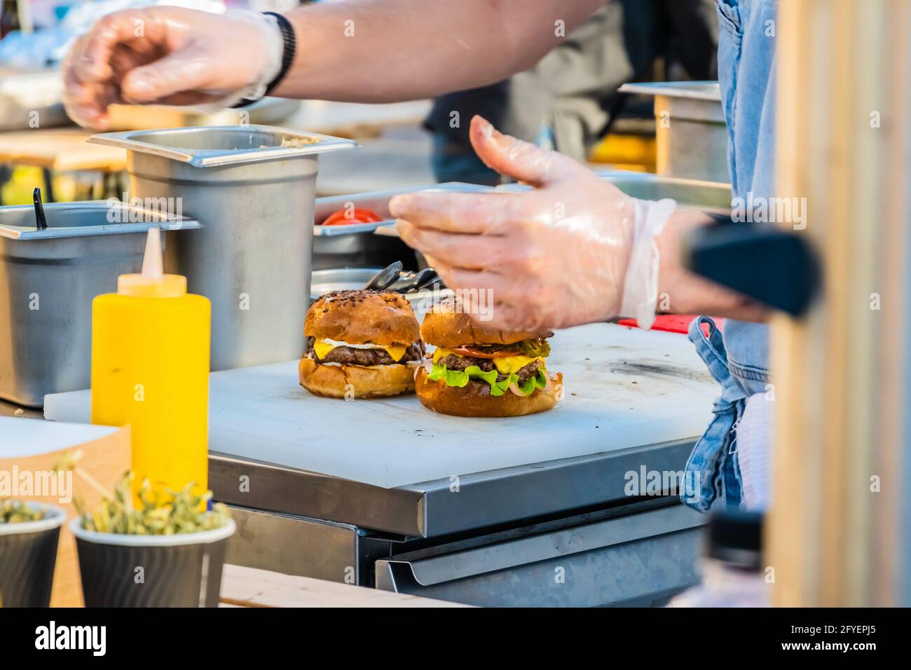 Ein professioneller Koch bereitet einen Burger zu. Zutaten für einen Burger. Grillfest im Stadtpark. Street Fast Food. Stockfoto