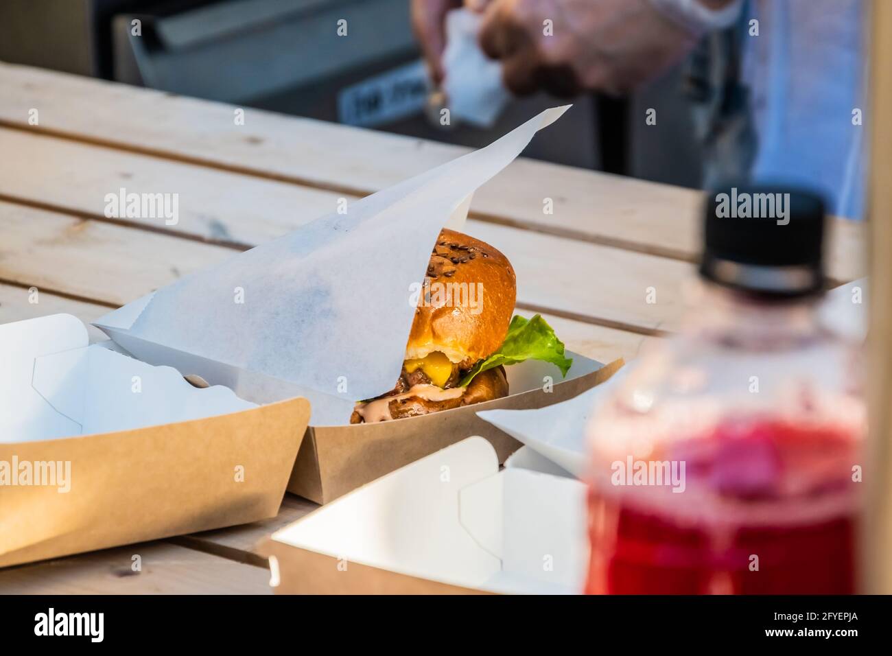 Saftiger Cheeseburger mit Rinderpasteten in einer Take-away-Verpackung auf der Theke eines Straßenhandels. Grillfest im Stadtpark. Street Fast Food. Stockfoto