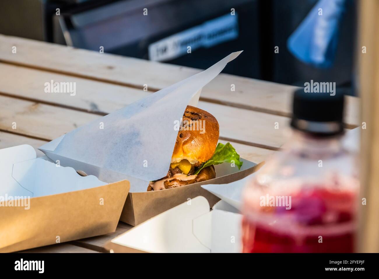 Saftiger Cheeseburger mit Rinderpasteten in einer Take-away-Verpackung auf der Theke eines Straßenhandels. Grillfest im Stadtpark. Street Fast Food. Stockfoto
