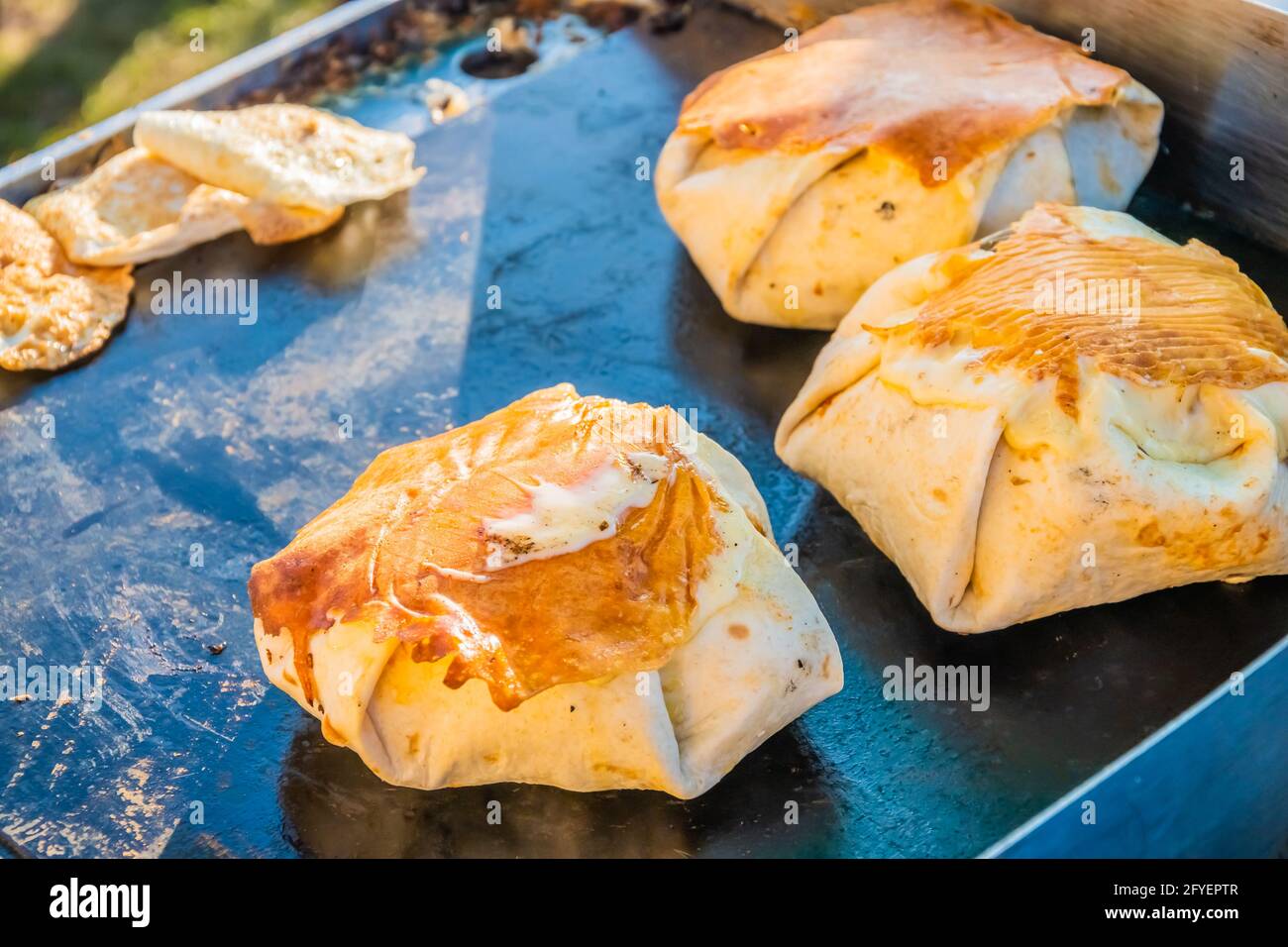 Mexikanisches Essen, ein Steak-Burger, der in einer Tortilla unter geschmolzenem Käse auf dem Grill eines Restaurants im Freien verpackt ist. Food Festival im Stadtpark. Straße f Stockfoto