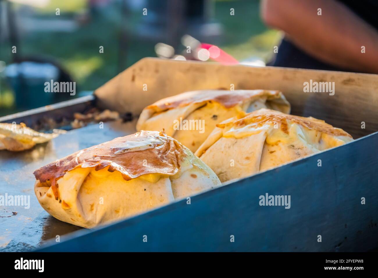 Mexikanisches Essen, ein Steak-Burger, der in einer Tortilla unter geschmolzenem Käse auf dem Grill eines Restaurants im Freien verpackt ist. Food Festival im Stadtpark. Straße f Stockfoto