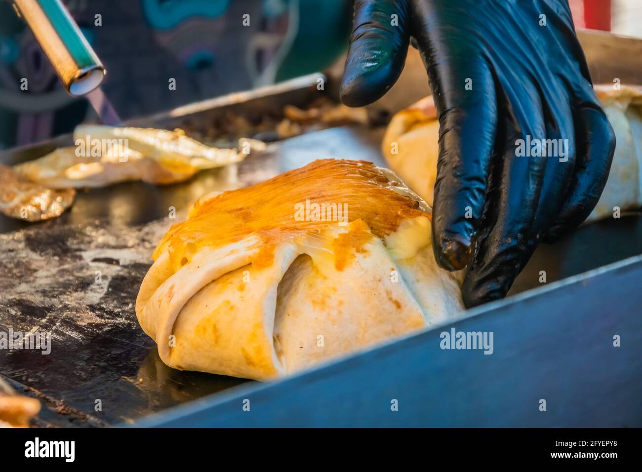 Mexikanisches Essen, ein Steak-Burger, der in einer Tortilla unter geschmolzenem Käse auf dem Grill eines Restaurants im Freien verpackt ist. Food Festival im Stadtpark. Straße f Stockfoto