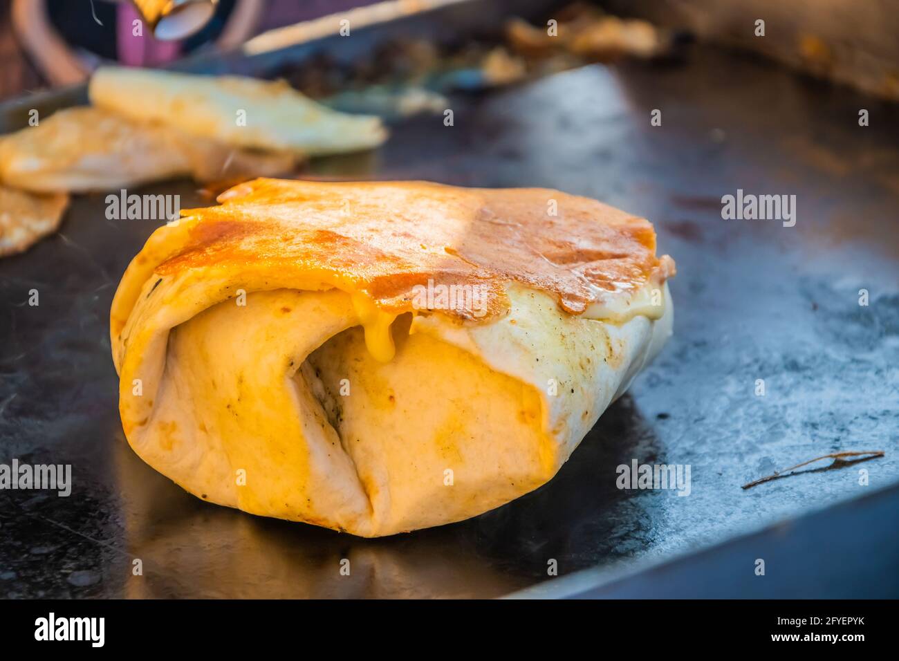 Mexikanisches Essen, ein Steak-Burger, der in einer Tortilla unter geschmolzenem Käse auf dem Grill eines Restaurants im Freien verpackt ist. Food Festival im Stadtpark. Straße f Stockfoto