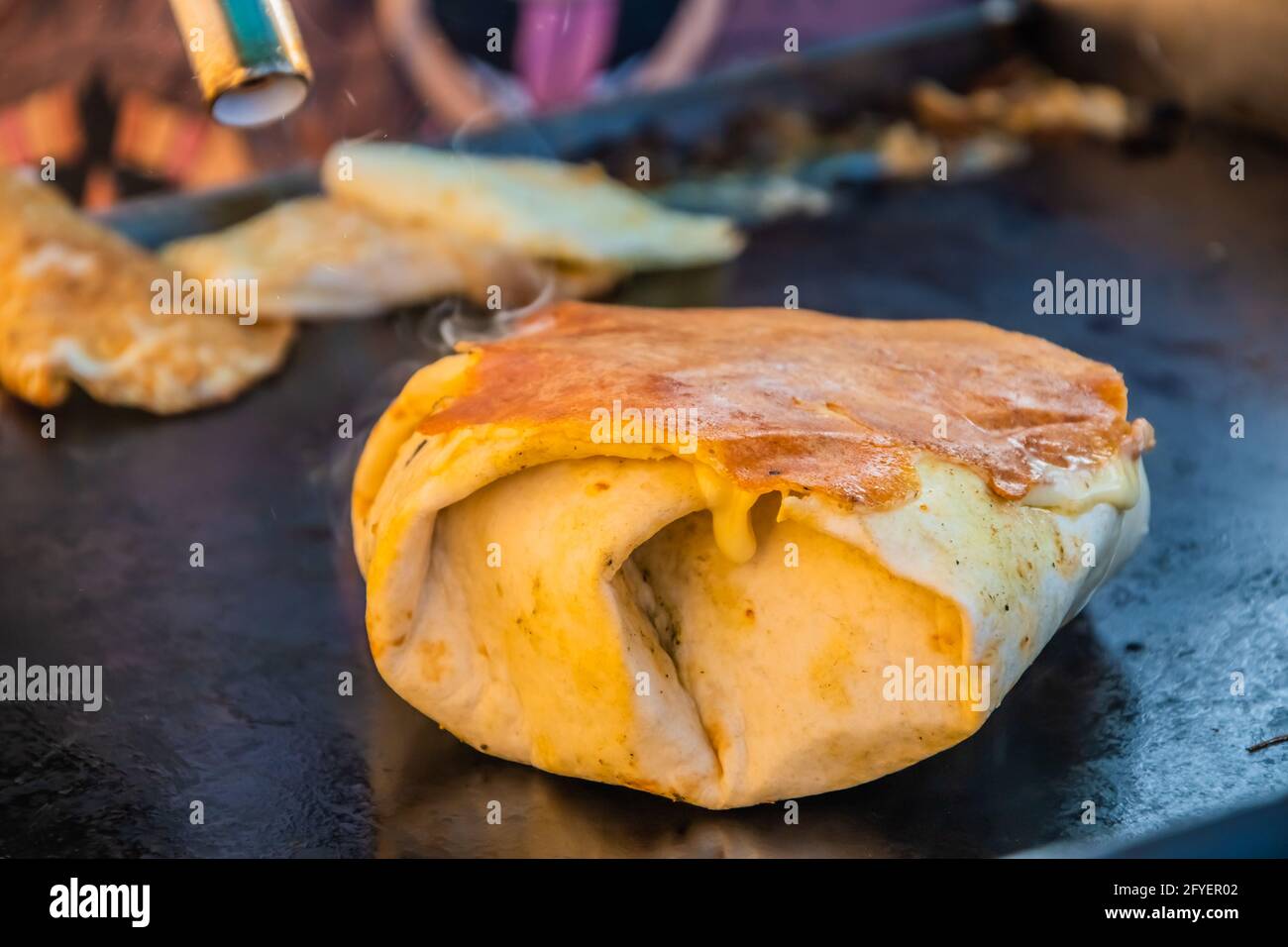 Mexikanisches Essen, ein Steak-Burger, der in einer Tortilla unter geschmolzenem Käse auf dem Grill eines Restaurants im Freien verpackt ist. Food Festival im Stadtpark. Straße f Stockfoto