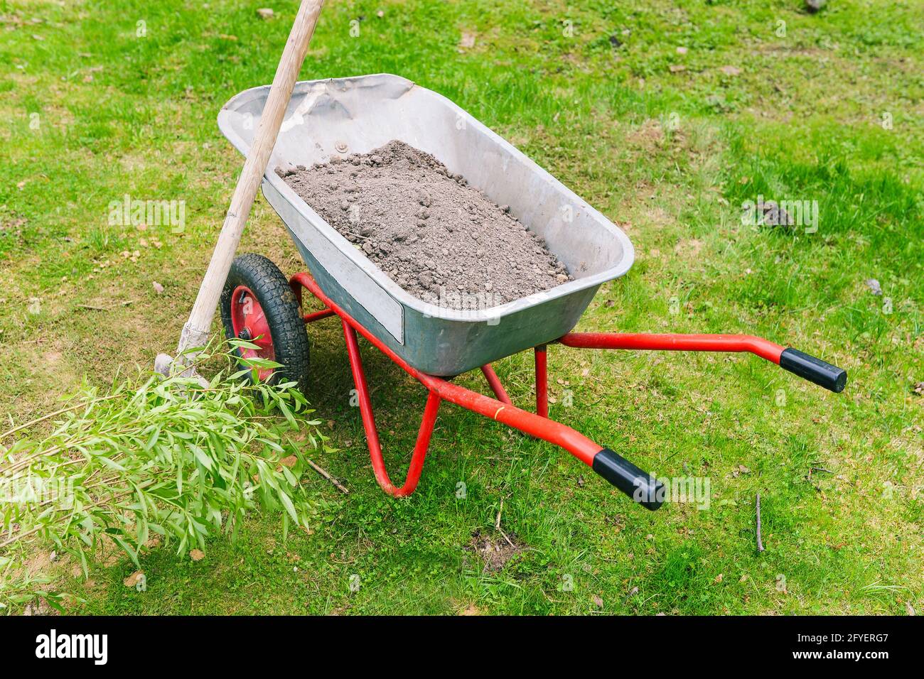 Gartenwagen mit Erde auf dem Rasen. Metallbauwagen für die Arbeit im Garten. Gärtnerwerkzeug mit Rädern für den Transport von Erde, Unkraut, SA Stockfoto