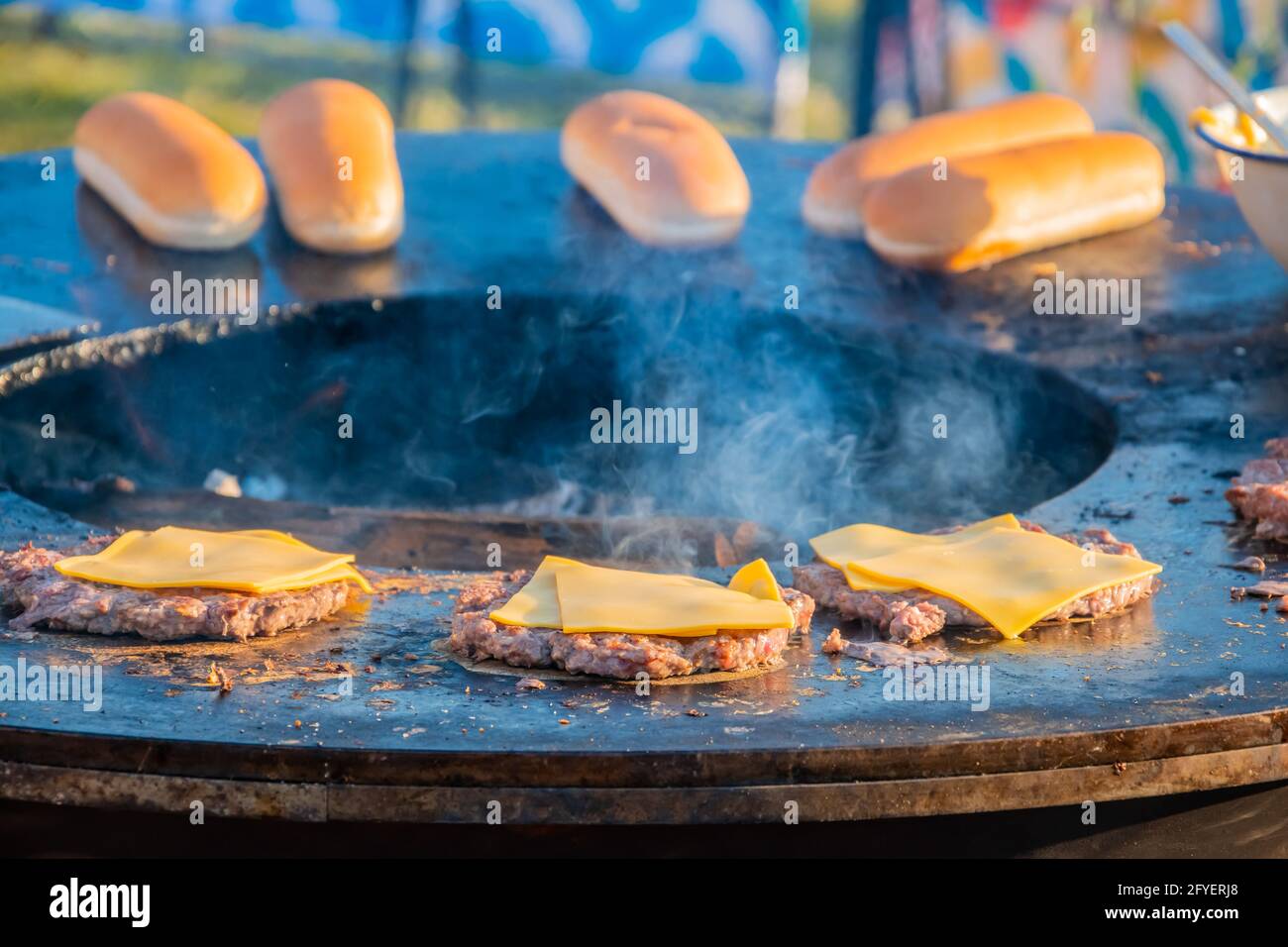 Auf dem Rasen röstet ein großer runder Holzgrill Rindersteaks für Burger. Der Koch dreht die gebratenen Koteletts um. Grillfest in der CI Stockfoto