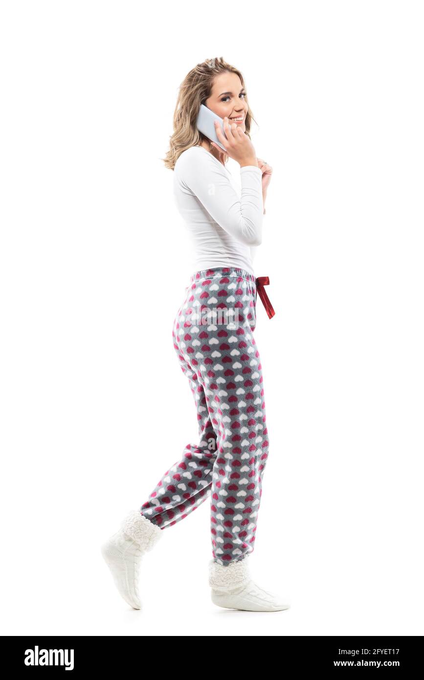 Seitenansicht einer glücklichen, entspannten Frau im Schlafanzug auf dem Handy, die die Kamera anlächelt. Ganzkörperlänge isoliert auf weißem Hintergrund. Stockfoto