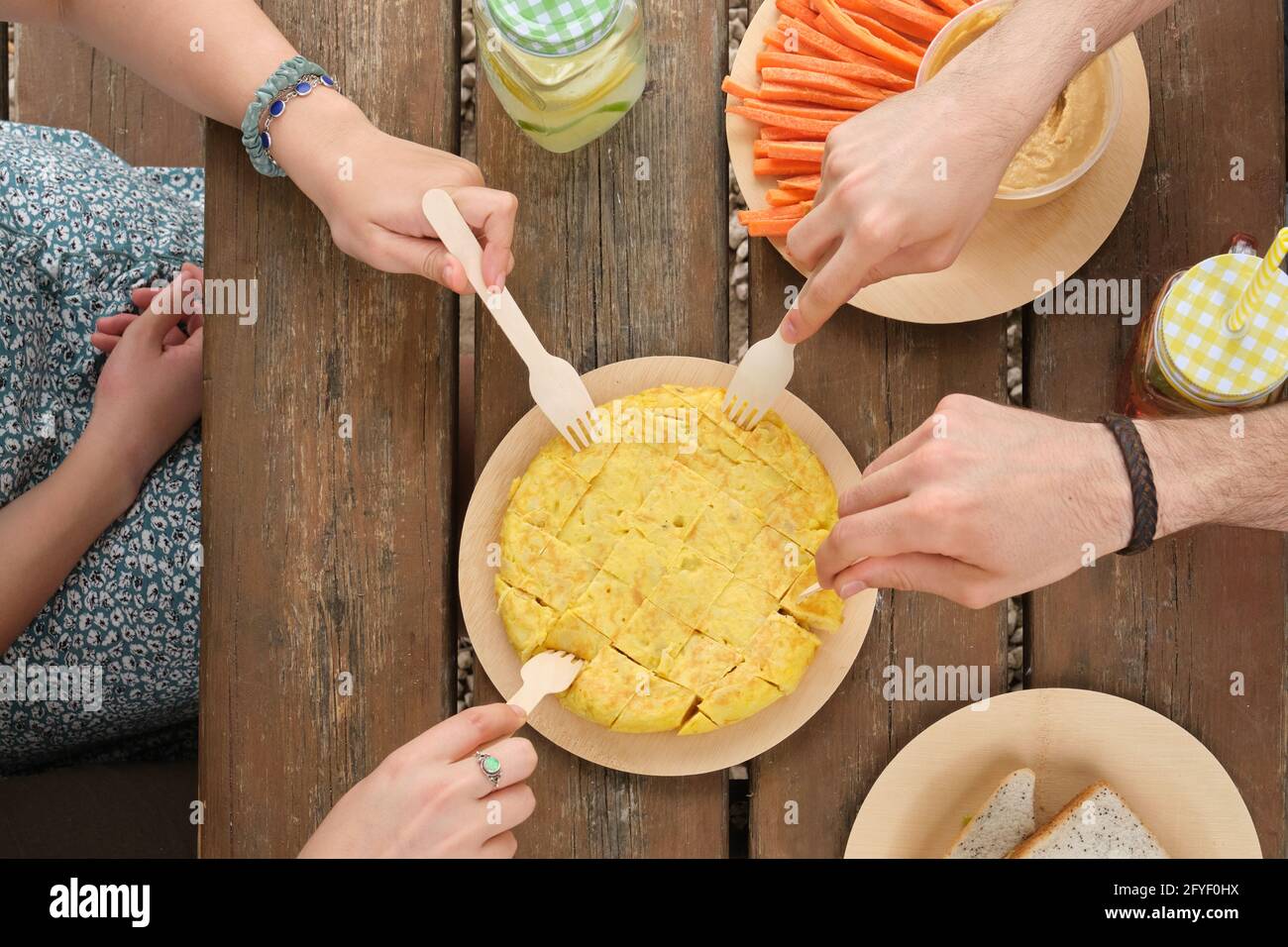 Eine Gruppe von unwiedererkennbaren, glücklichen Freunden, die an einem sonnigen Sommertag ein Stück spanisches Omelett mit einer Gabel in einem Park zum Picknick nehmen. Draufsicht. Stockfoto
