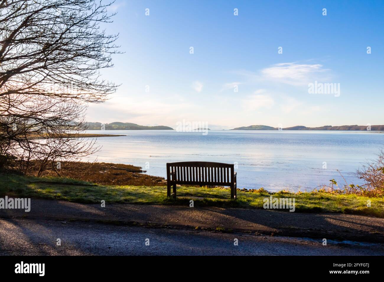 Ein leerer Holzsitz oder eine Bank mit Blick auf das Meer in der Kirkcudbright Bay, bei Ebbe an einem sonnigen Wintermorgen, Dumfries und Galloway, Schottland Stockfoto