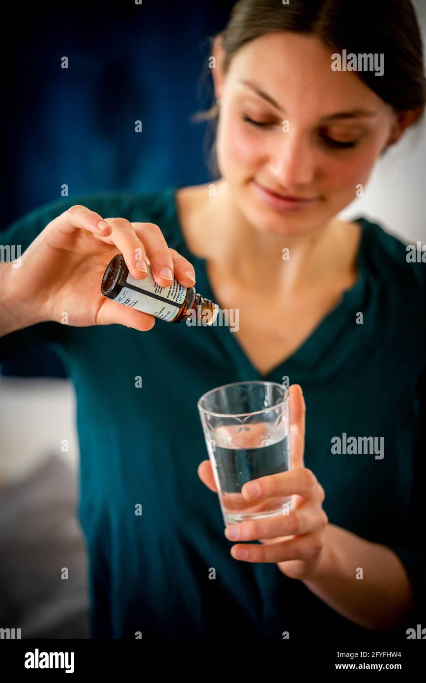 Frau gießt Tropfen mazeratem Knospen in ein Glas Wasser. Stockfoto