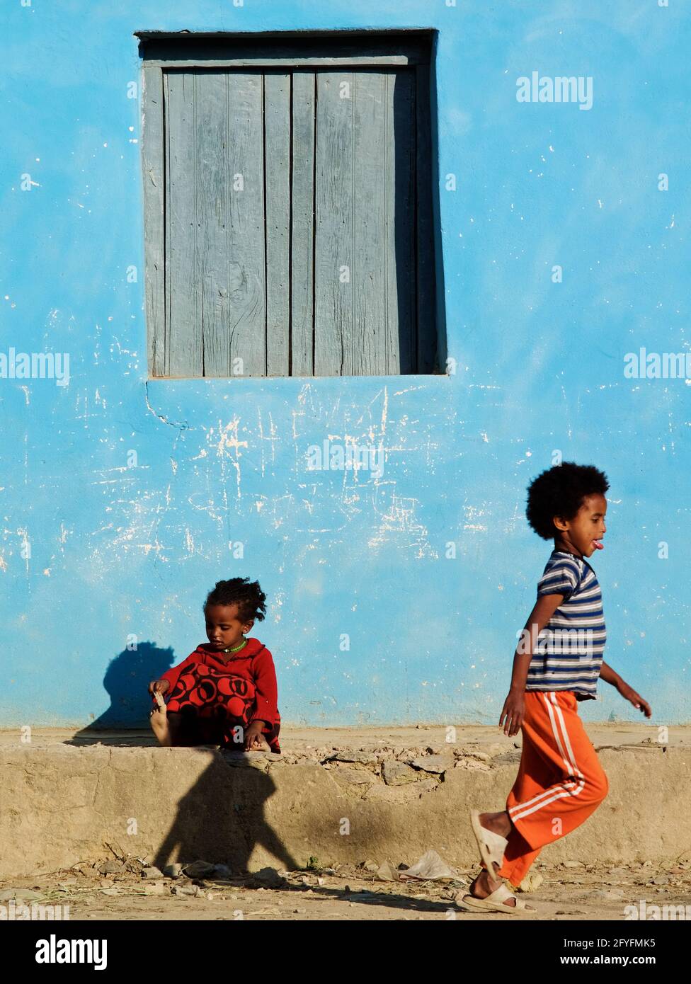 Zwei äthiopische Kinder spielen, ein Junge läuft und ein kleines Mädchen sitzt vor einem bunten Haus im Dorf Atsbi, Tigray, Äthiopien Stockfoto