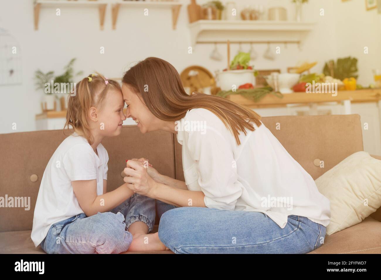 Das vertrauensvolle Verhältnis von Mutter und Tochter. Gespräch einer Frau mit einem kleinen Mädchen zu Hause auf der Couch in der Küche. Beste Freunde glücklich Motte Stockfoto