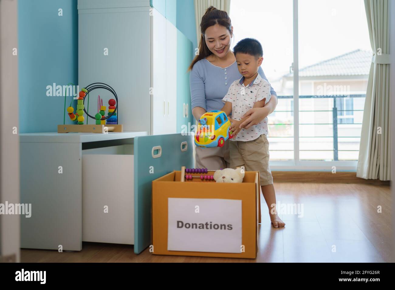 Asiatische Mutter und Sohn wählen das Spielzeug ihrer Kinder, das nicht spielt, und legen Spendenboxen an das Spendenzentrum. Stockfoto