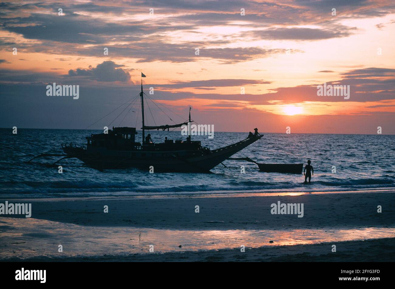 Philippinen. Region Luzon. Strand bei Sonnenuntergang. Fischerboot und Fischer silhouetted. Stockfoto