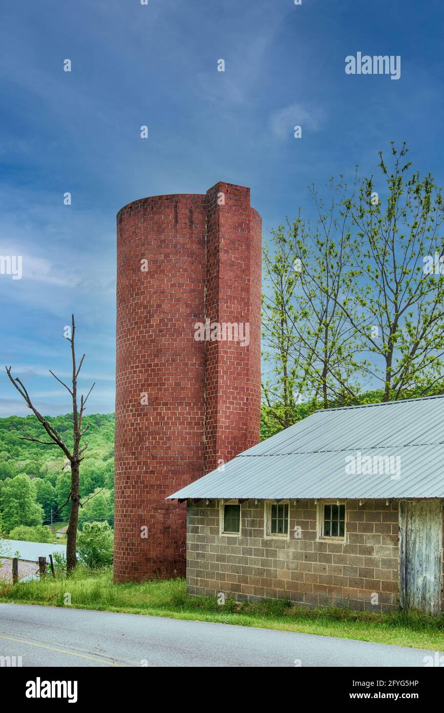 Altes Ziegelsilo vor einem wunderschönen blauen Himmel neben einem Blockgebäude. Stockfoto