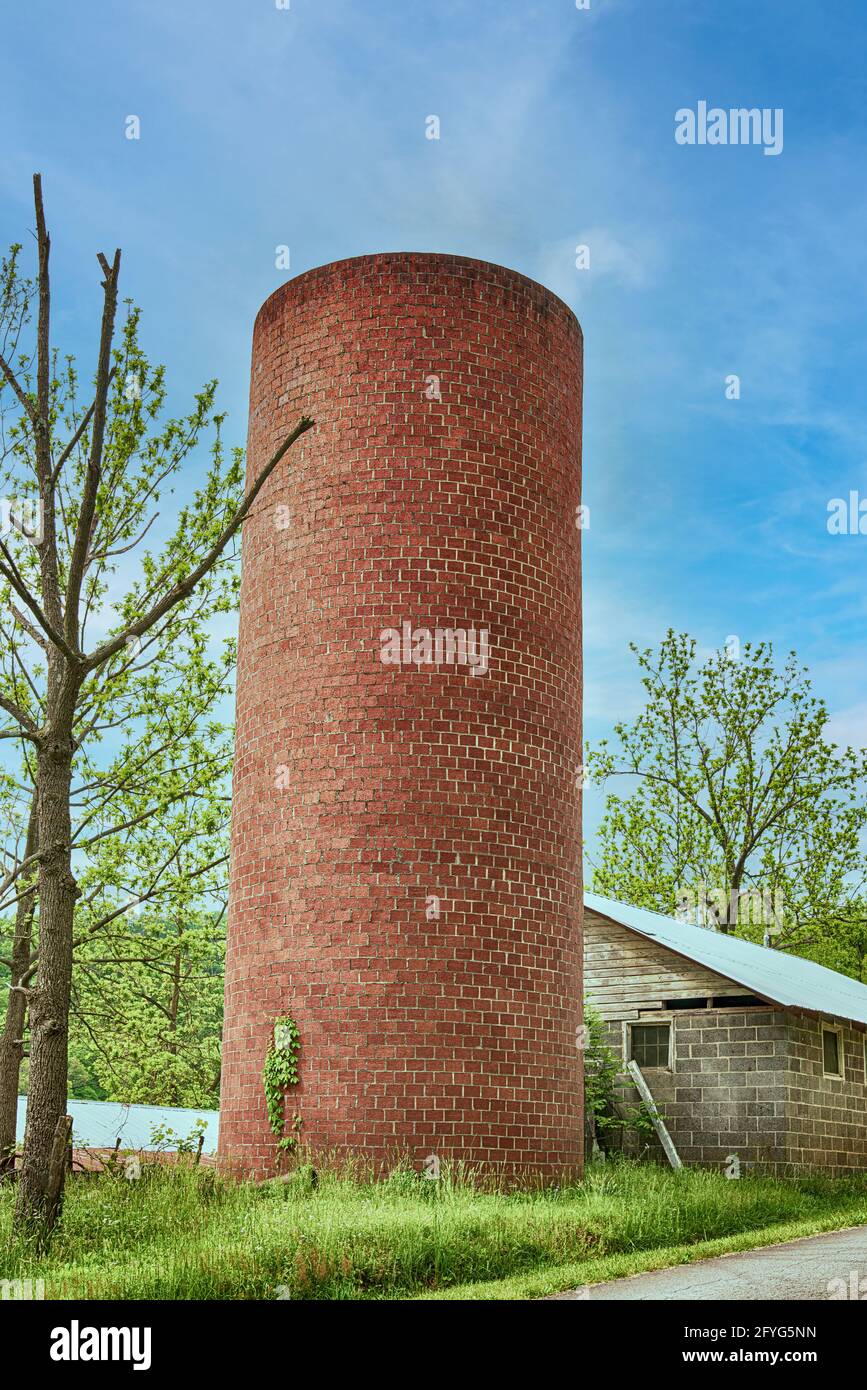 Altes Ziegelsilo vor einem wunderschönen blauen Himmel neben einem Blockgebäude. Stockfoto