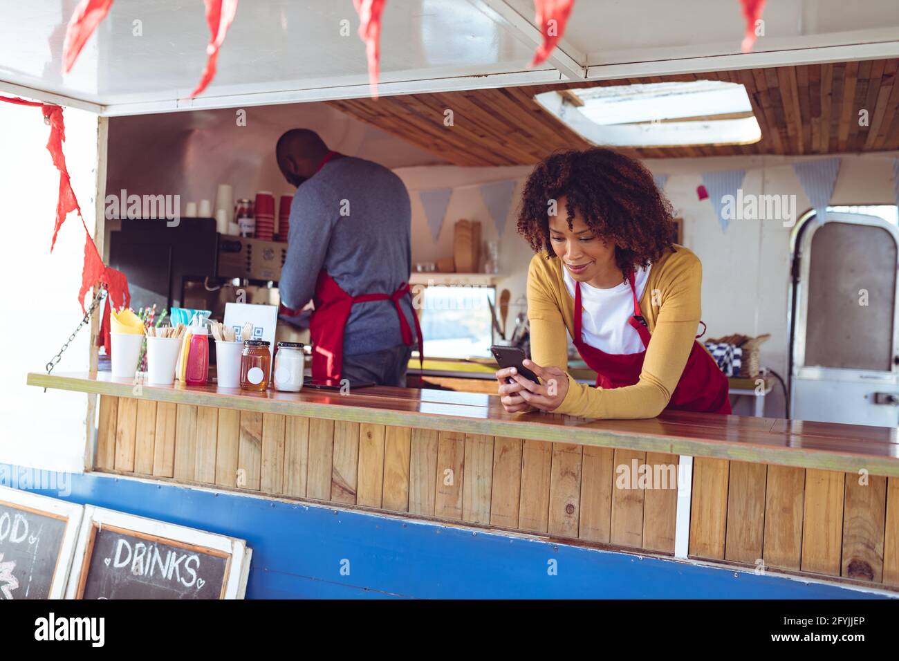 Frau mit gemischter Rasse und Smartphone, die sich im Essen auf der Theke lehnt LKW Stockfoto