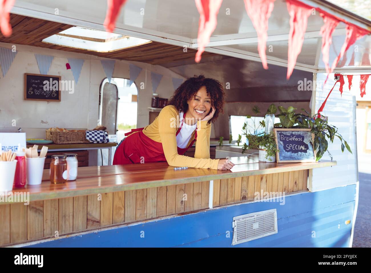 Porträt einer lächelnden Frau mit gemischter Rasse, die sich an der Theke lehnt Foodtruck Stockfoto