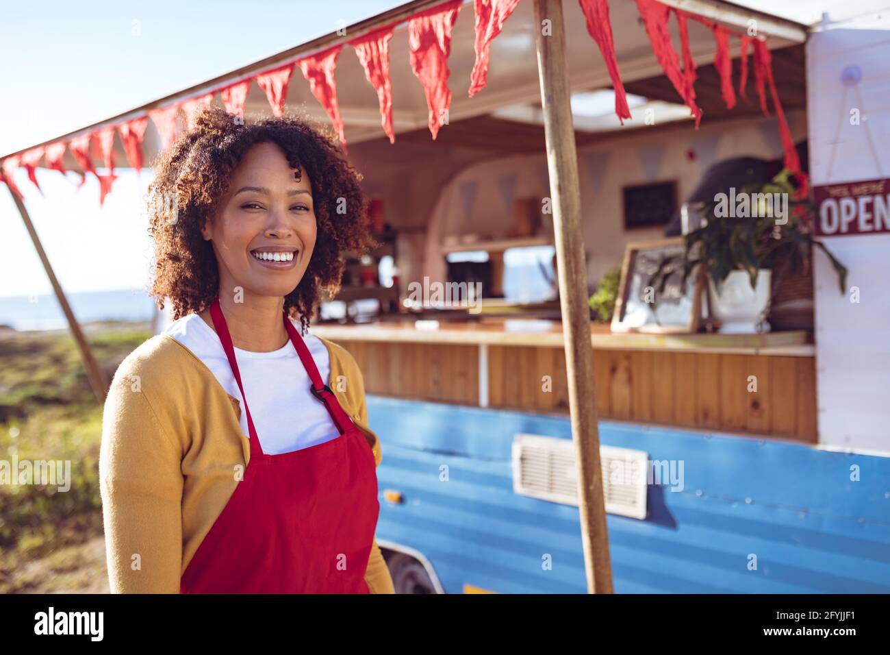 Porträt einer lächelnden Frau mit gemischter Rasse, die neben einem Food Truck steht An einem sonnigen Tag Stockfoto