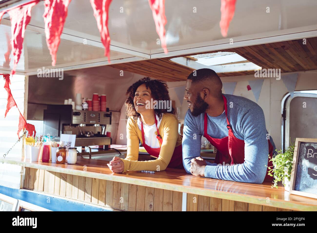 Lächelndes, vielfältiges Paar hinter dem Tresen in einem Food Truck auf der Sonnenseite Tag Stockfoto