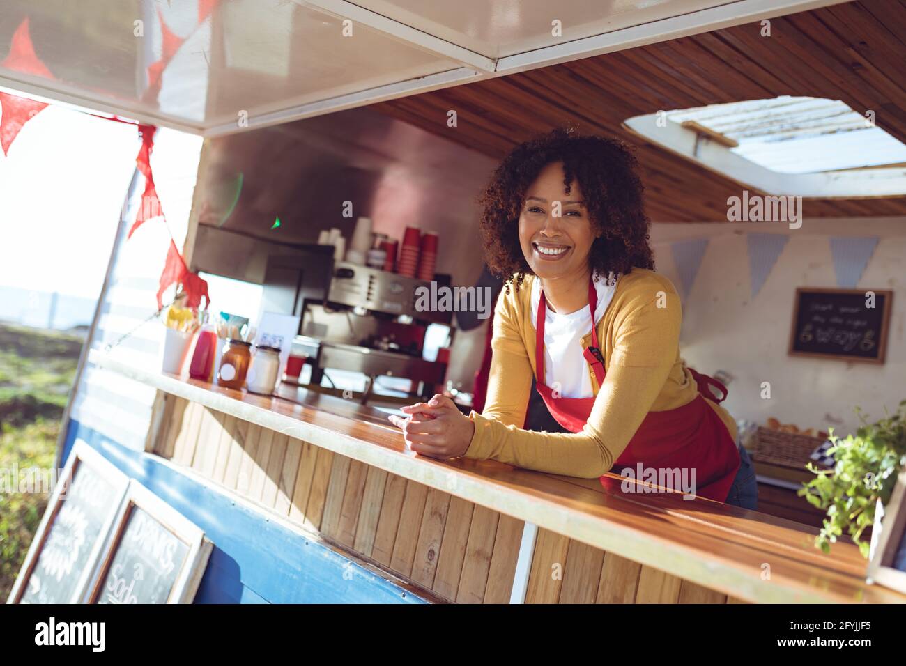 Porträt einer lächelnden Frau mit gemischter Rasse, die sich an der Theke lehnt Foodtruck Stockfoto