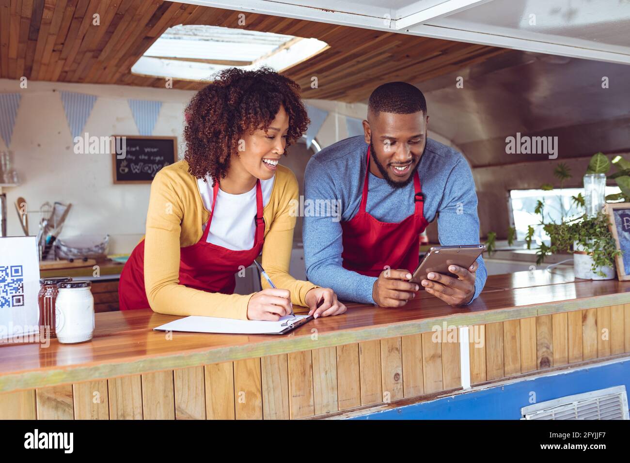 Lächelndes, vielfältiges Paar hinter dem Ladentisch mit Tablet im Food Truck Stockfoto