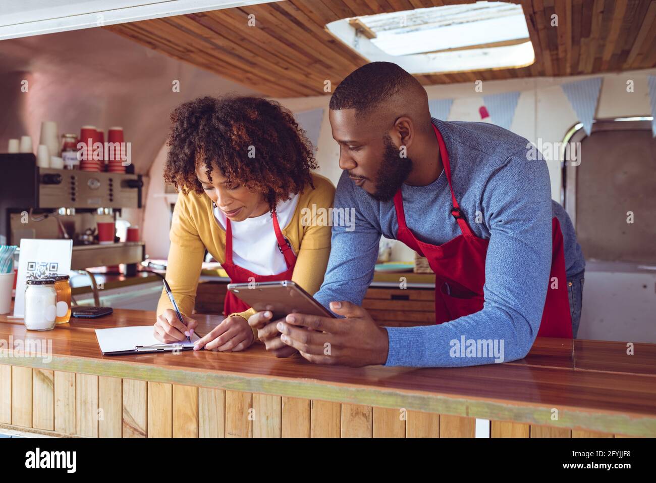 Lächelndes, vielfältiges Paar hinter dem Tresen, das Tablet benutzte und einschrieb Foodtruck Stockfoto