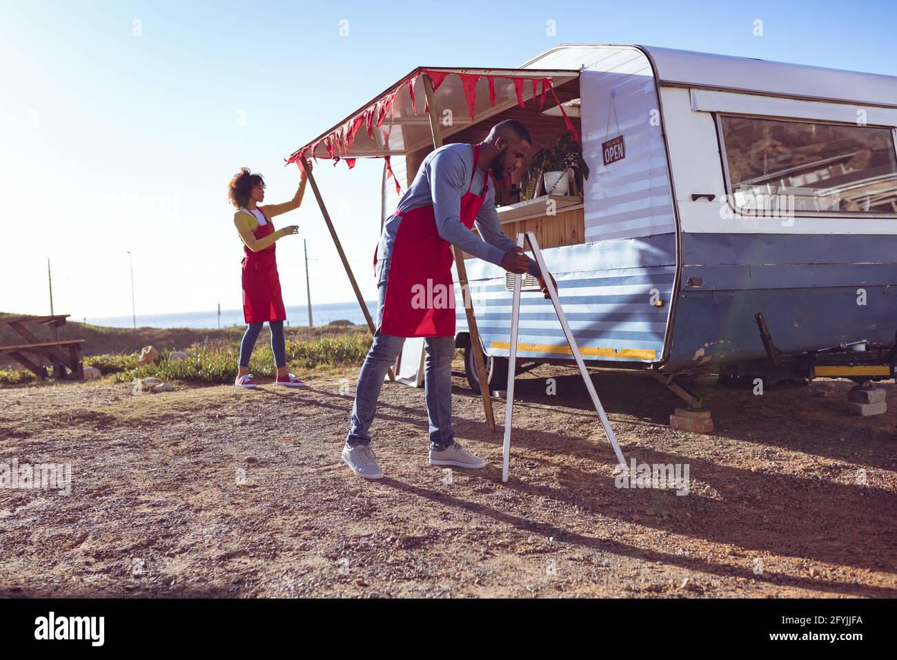 Diverse Paare öffnen und bereiten Food Truck von Seaside on Sonniger Tag Stockfoto
