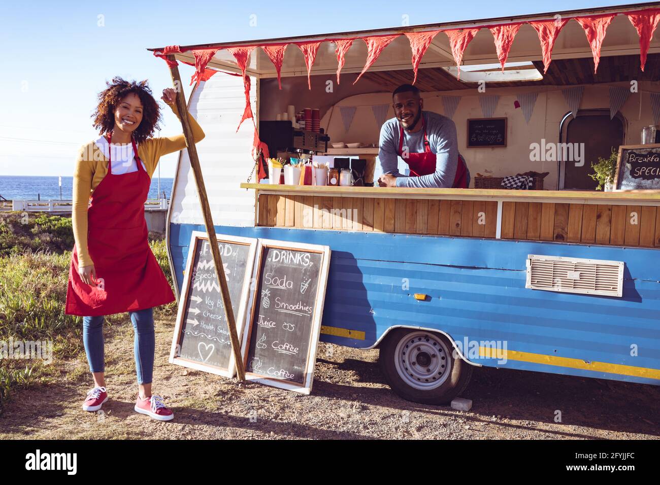 Porträt eines lächelnden, vielfältigen Paares in einem Food Truck am Meer Stockfoto
