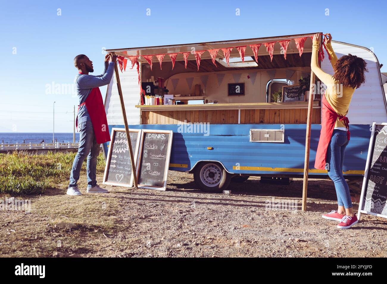 Diverse Paare öffnen und bereiten Food Truck von Seaside on Sonniger Tag Stockfoto