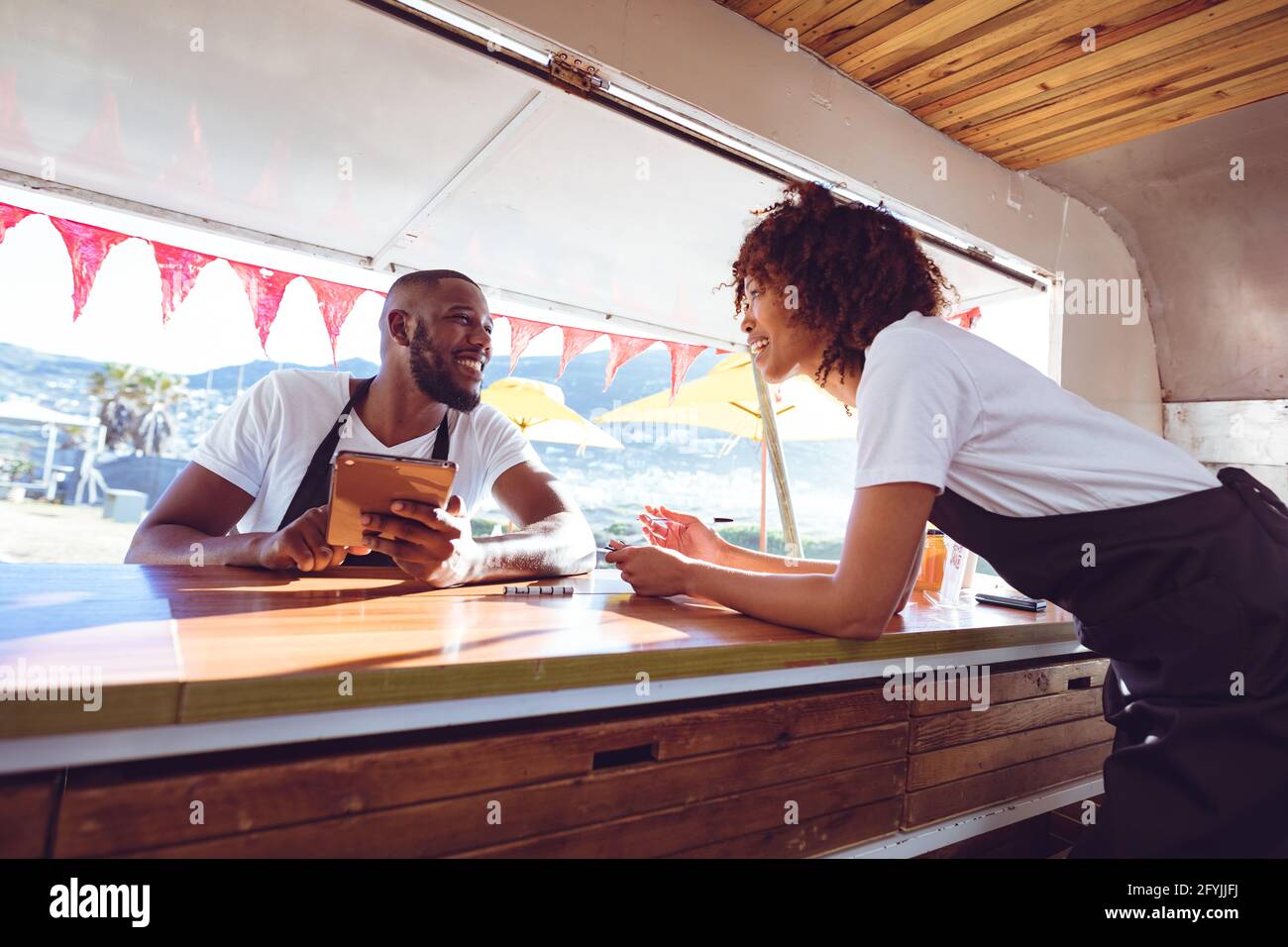 Lächelndes, vielfältiges Paar, das sich auf der Theke mit einer Tablette in der Nahrung stützt LKW Stockfoto