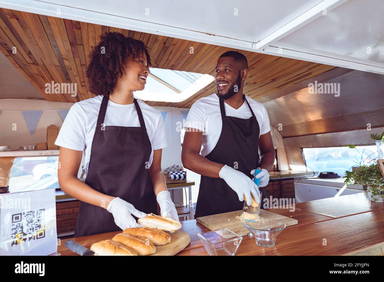 Lächelndes, vielfältiges Paar, das hinter dem Tresen Hotdogs in Essen zubereitete LKW Stockfoto