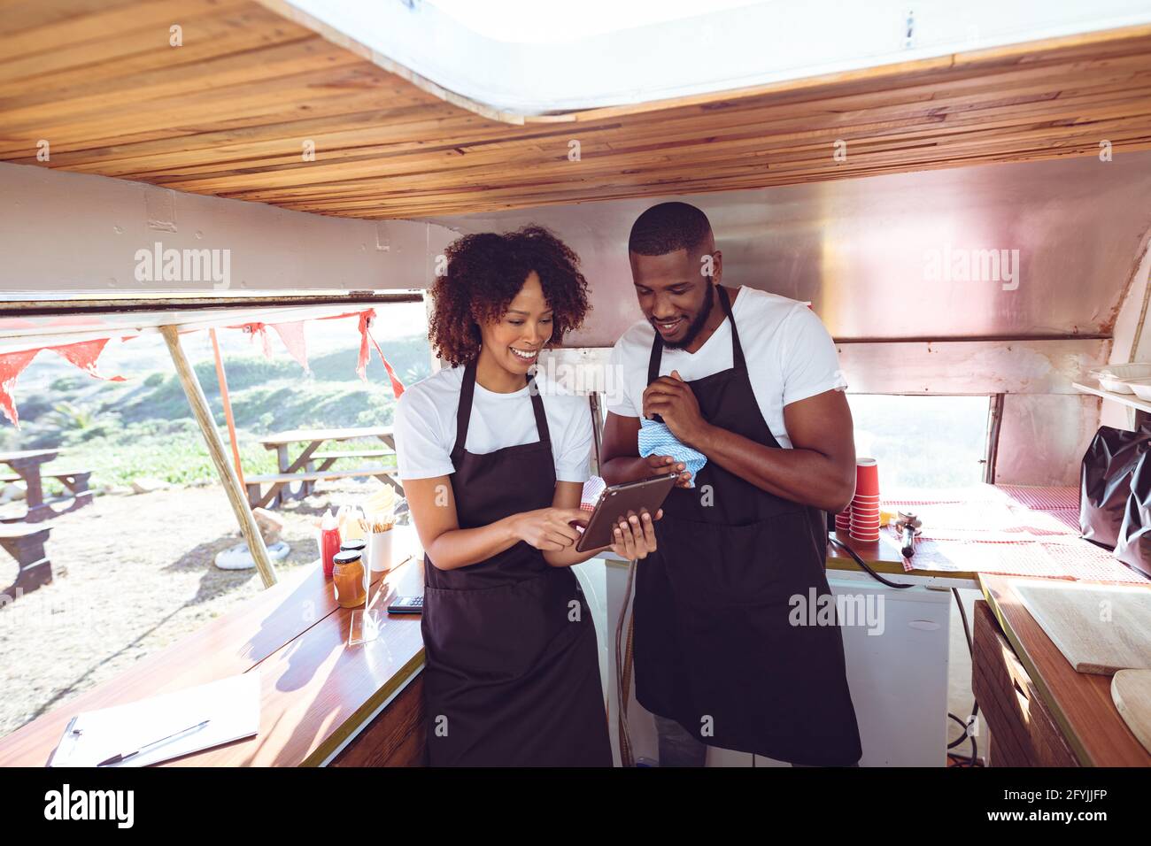 Lächelndes, vielfältiges Paar hinter dem Ladentisch mit Tablet im Food Truck Stockfoto