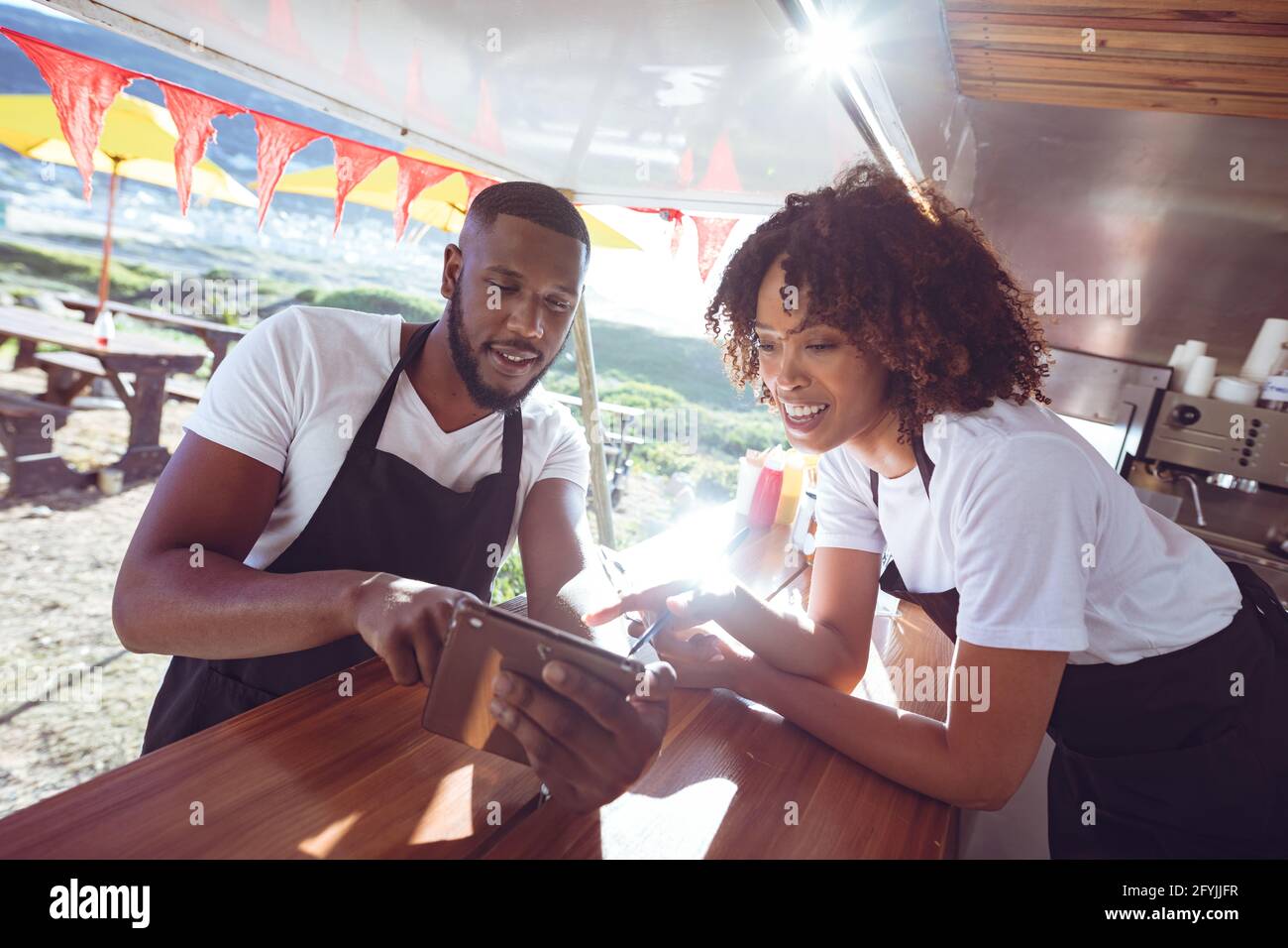 Lächelndes, vielfältiges Paar, das sich auf der Theke mit einer Tablette in der Nahrung stützt LKW Stockfoto