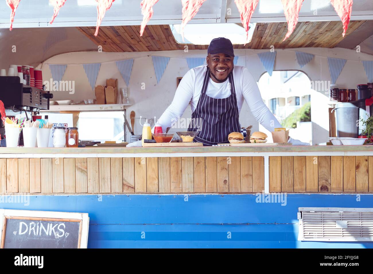 Porträt eines lächelnden afroamerikanischen Mannes in einem Food Truck mit Hamburger auf der Arbeitsplatte Stockfoto