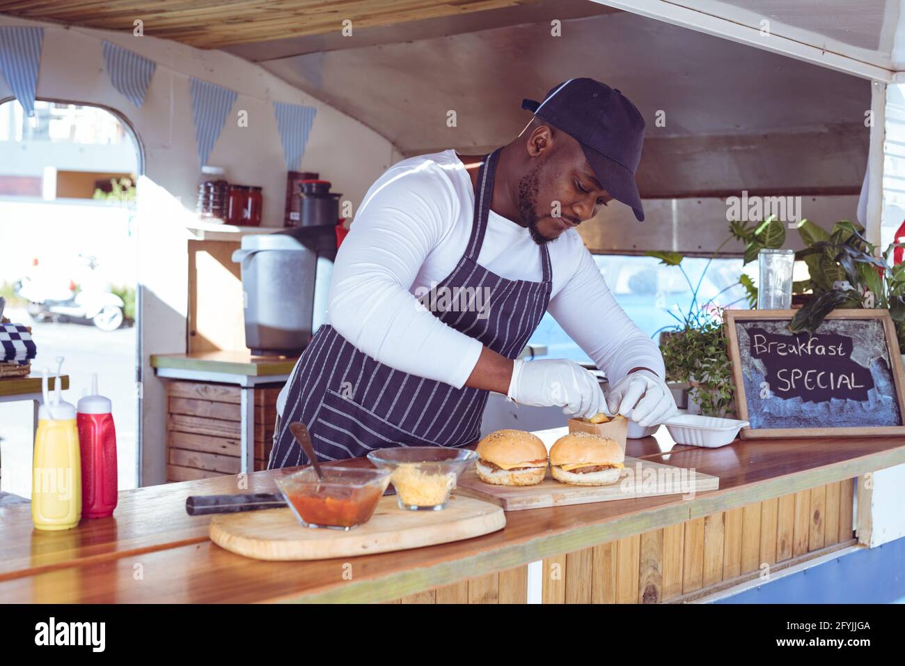 Afroamerikanischer Mann im Food Truck, der Ordnung mit Hamburgern vorbereitet Auf der Arbeitsplatte Stockfoto