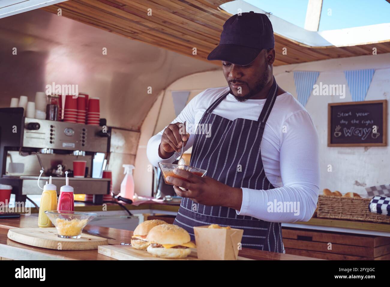 Afroamerikanischer Mann im Food Truck, der Ordnung mit Hamburgern vorbereitet Auf der Arbeitsplatte Stockfoto