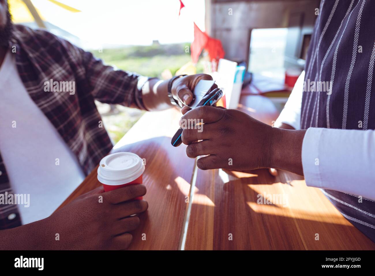 Mittelteil des afroamerikanischen Mannes in Food Truck mit Smartphone Zahlungsterminal Stockfoto
