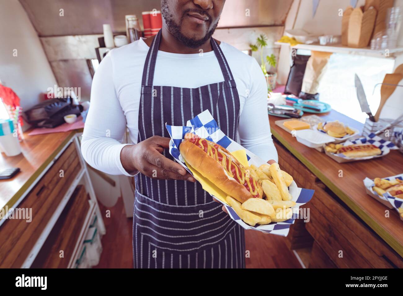 Mittelteil eines afroamerikanischen Mannes in einem Food Truck, der Hotdog hält Und Chips Stockfoto