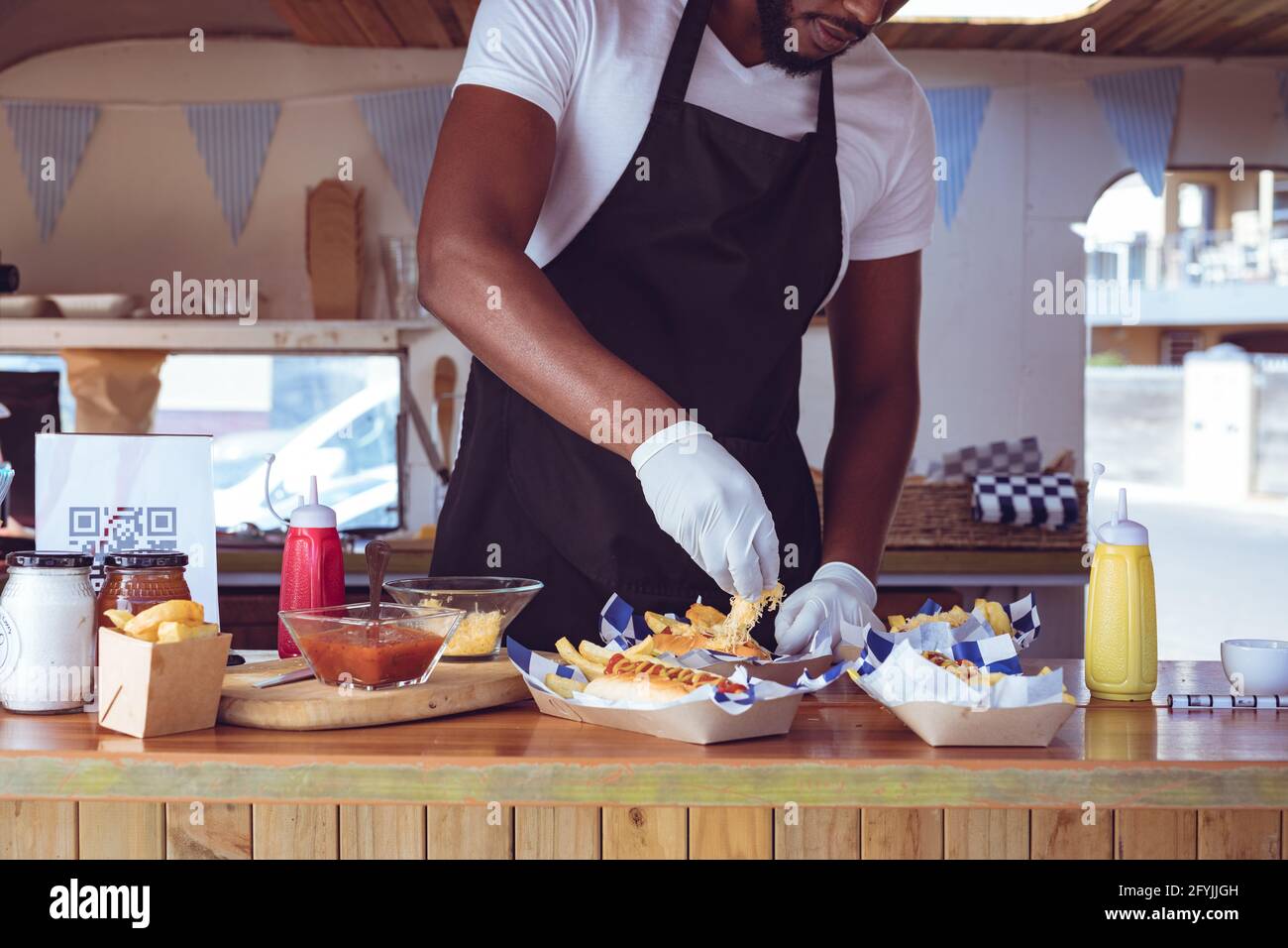 Mittelteil des afroamerikanischen Mannes im Food Truck, der die Bestellung vorbereitet Mit Hotdogs auf der Arbeitsplatte Stockfoto