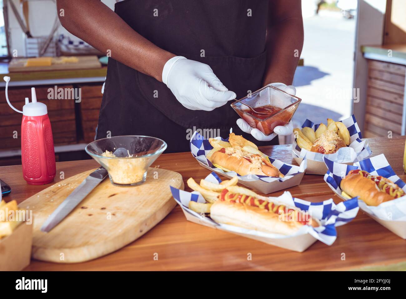 Mittelteil eines afroamerikanischen Mannes in einem Lastwagen mit Ketchup Gericht mit Hotdogs auf der Arbeitsplatte Stockfoto