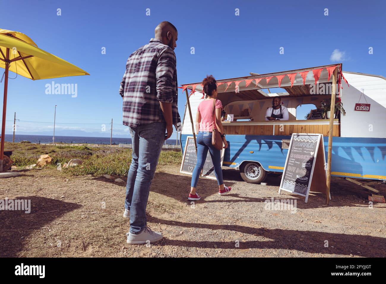 Lächelnder afroamerikanischer Mann in einem Food Truck, der darauf wartet, es zu nehmen Bestellung von weiblicher Kundin Stockfoto