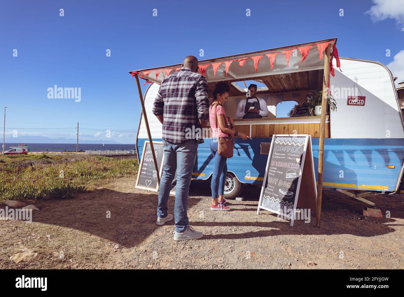 Lächelnder afroamerikanischer Mann in einem Food Truck, der die Bestellung von abnimmt Weibliche Kundin Stockfoto