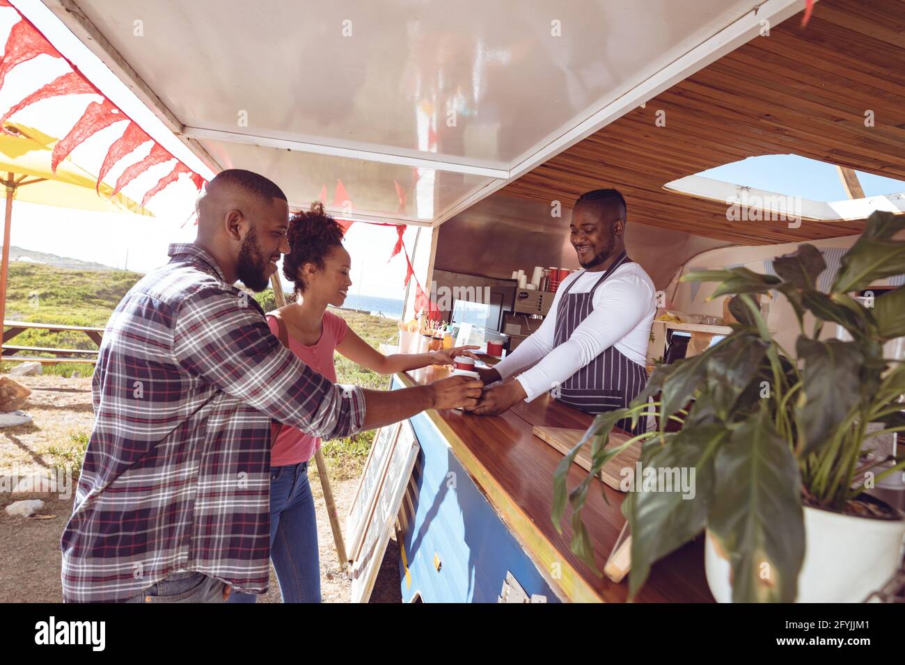 Lächelnder afroamerikanischer Mann im Food Truck, der mit dem Mann plaudert Und weiblichen Kunden Stockfoto
