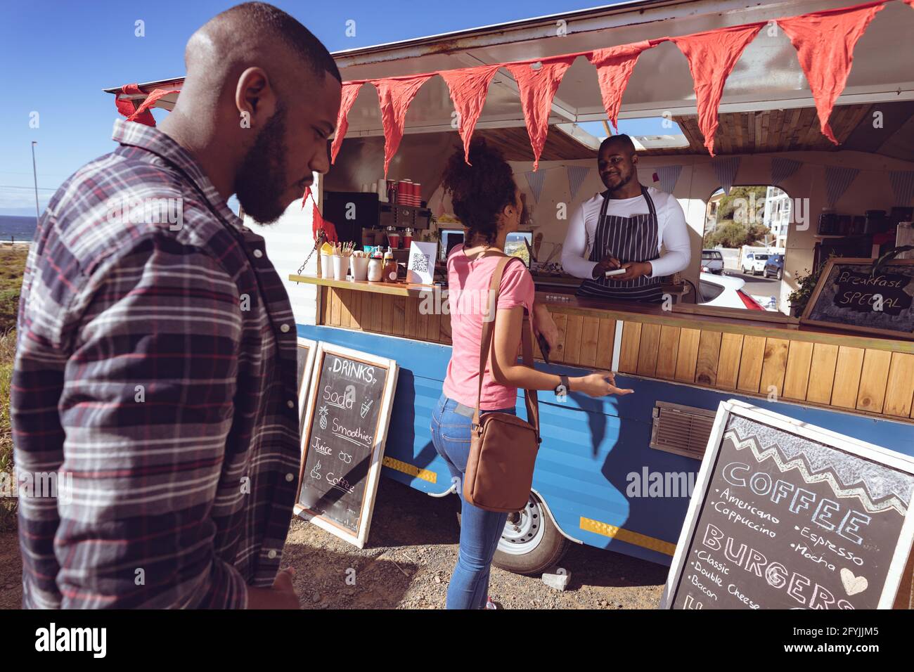 Lächelnder afroamerikanischer Mann in einem Food Truck, der die Bestellung von abnimmt Weibliche Kundin Stockfoto