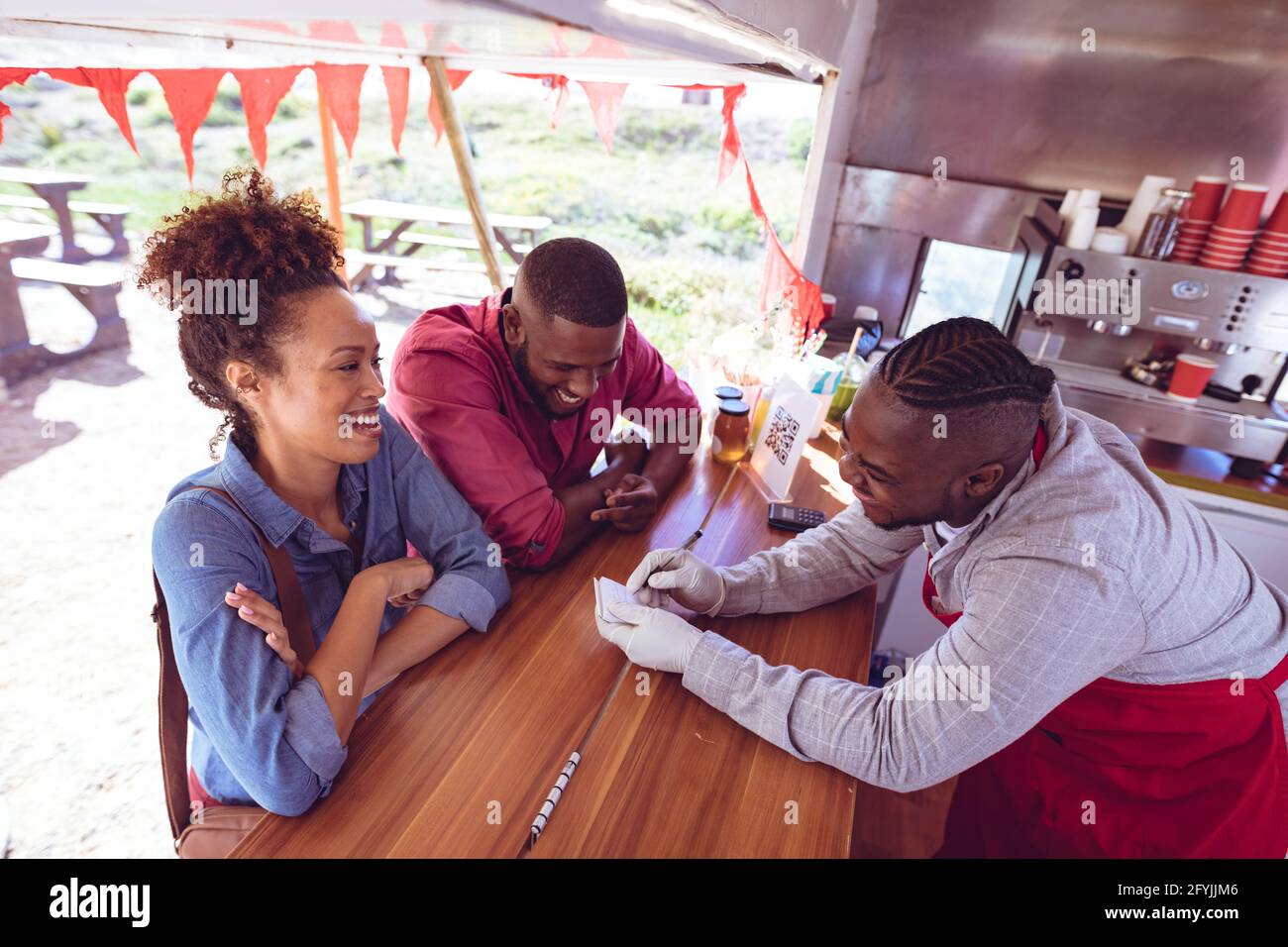 Lächelnder afroamerikanischer Mann im Food Truck, der mit dem Mann plaudert Und weiblichen Kunden Stockfoto