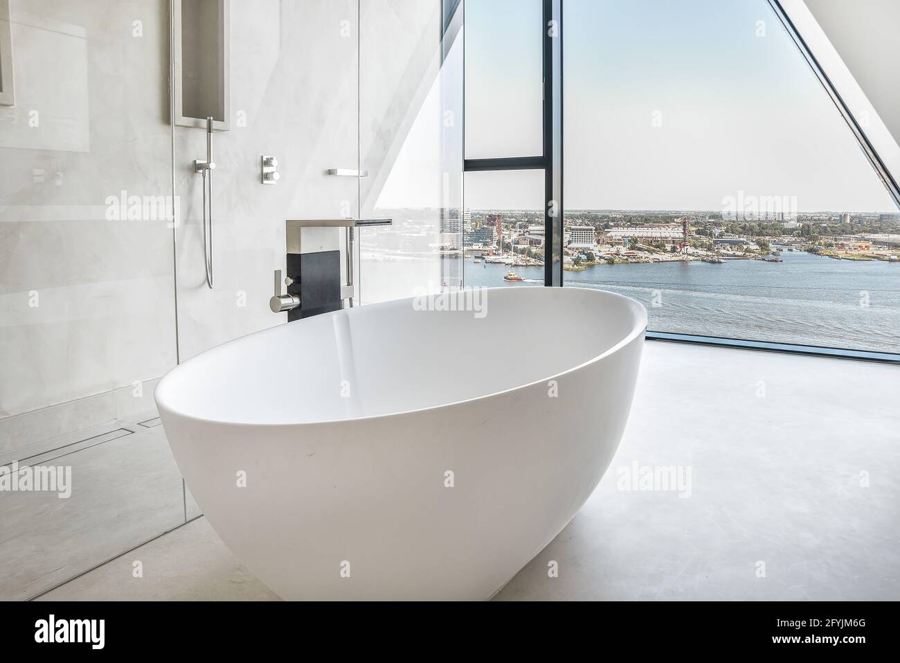 Große weiße Badewanne im geräumigen Badezimmer mit Duschkabine Und Fenster mit Blick auf die Stadt Stockfoto